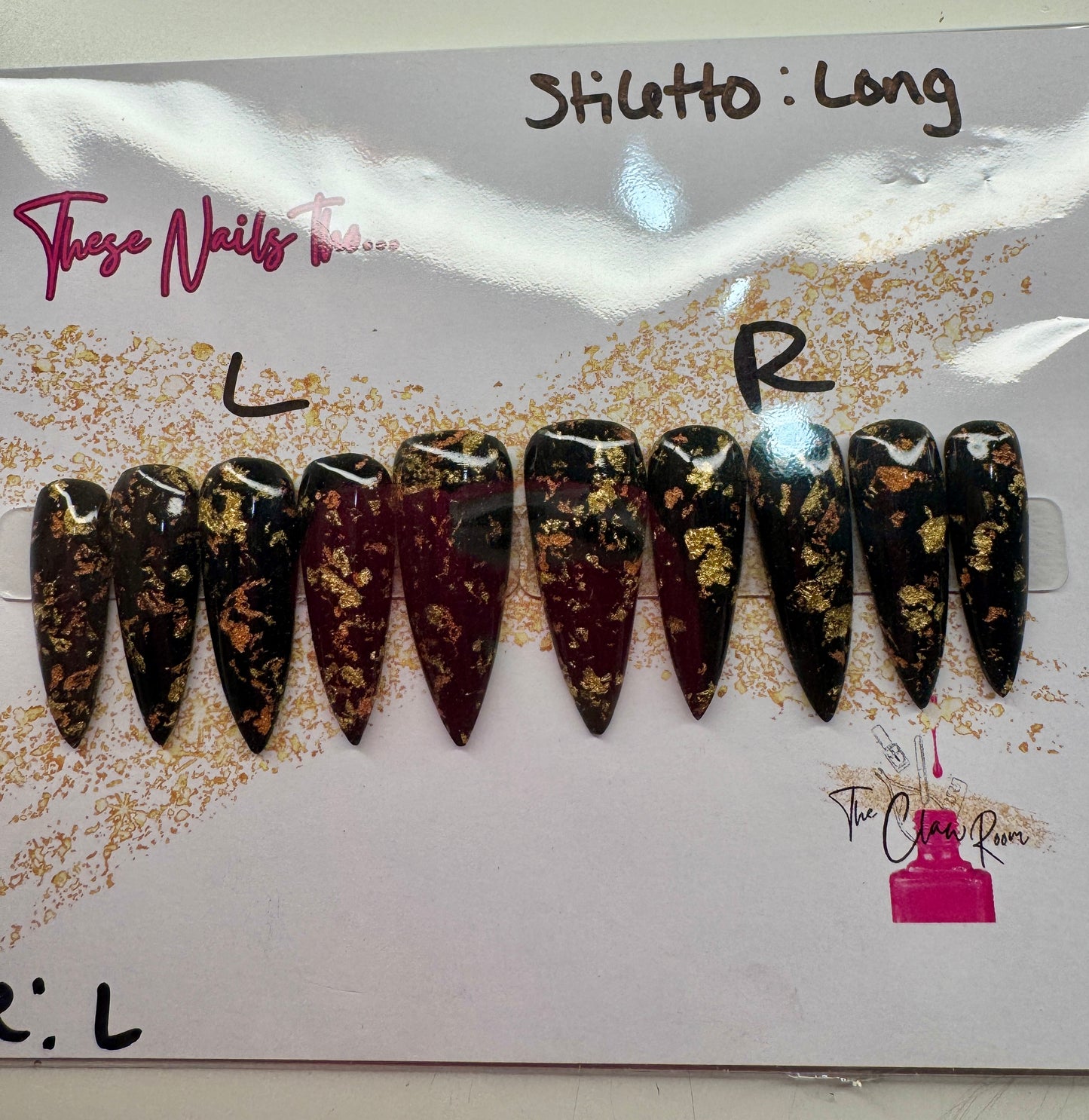 Long stiletto press-on nail set featuring a rich black and burgundy base with scattered gold foil accents. Nails are glossy and dramatic, exuding a luxe, edgy vibe.