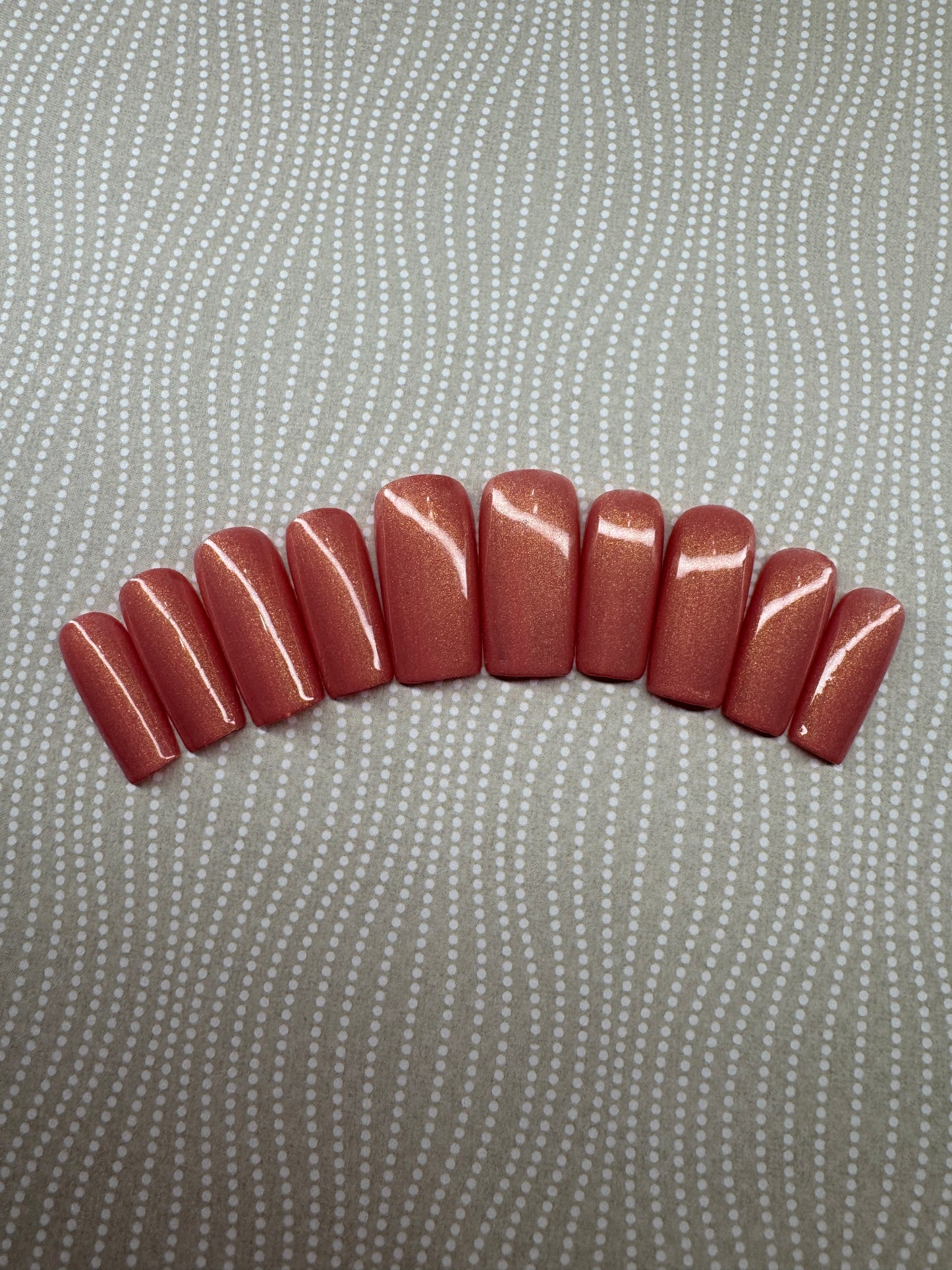 Set of medium square press-on nails in a vibrant coral shade with a golden shimmer finish, displayed on a branded card with glitter background.