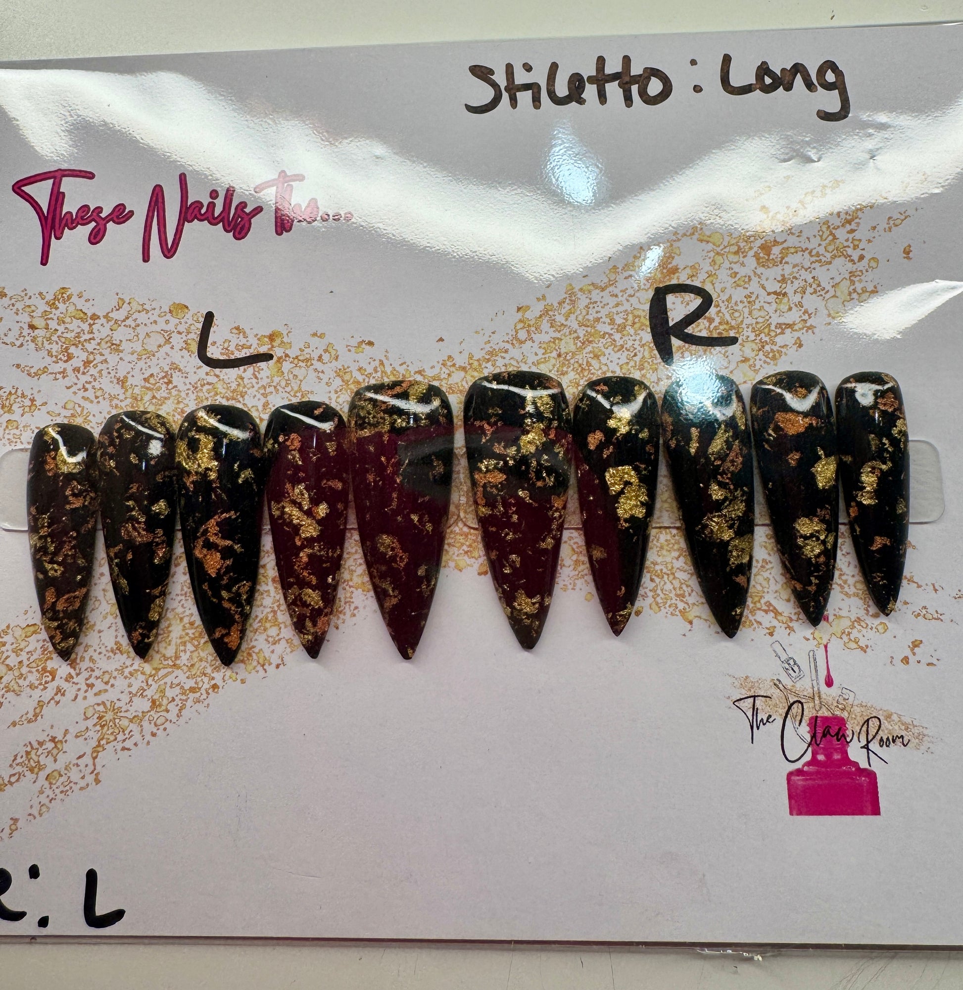 Long stiletto press-on nail set featuring a rich black and burgundy base with scattered gold foil accents. Nails are glossy and dramatic, exuding a luxe, edgy vibe.