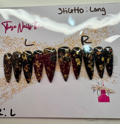 Long stiletto press-on nail set featuring a rich black and burgundy base with scattered gold foil accents. Nails are glossy and dramatic, exuding a luxe, edgy vibe.